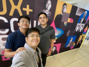 Three team members taking a selfie in front of UX+ Conference backdrop